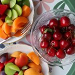 Vibrant mix of fresh summer fruits in decorative bowls on a floral patterned tray.
