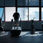 A man exercises on a treadmill in a modern gym overlooking a city skyline.